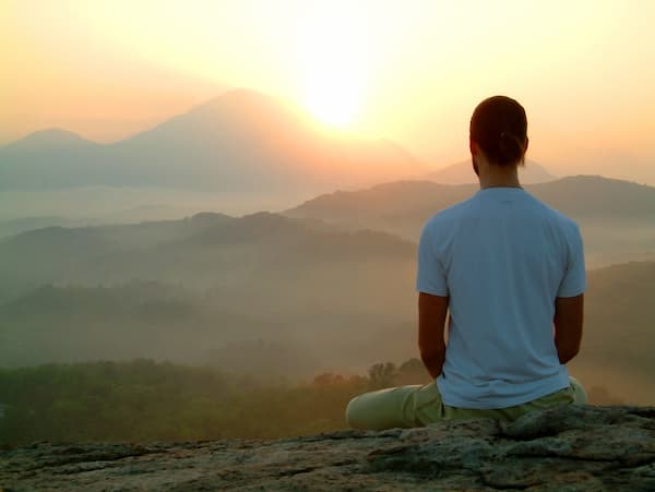Person meditating at sunrise representing mindfulness and emotional wellness